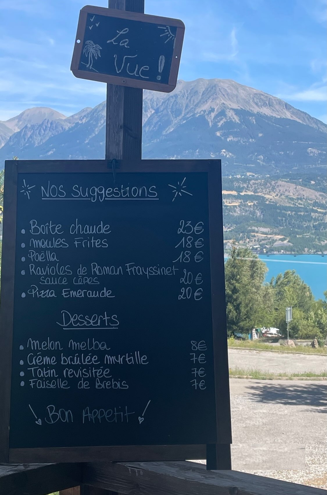 L'ardoise des suggestions du jour devant les montagnes et le lac